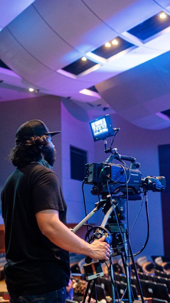 A videographer operates a camera capturing a large event indoors.